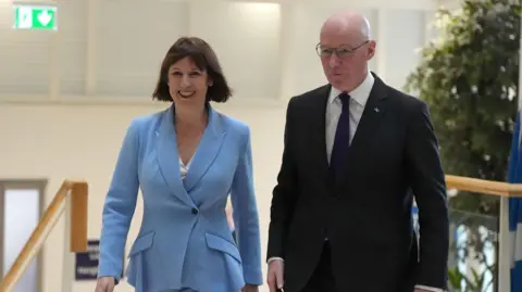 PA Media Rachel Reeves and John Swinney walking together. Both are smiling as the Chancellor visits Scotland.